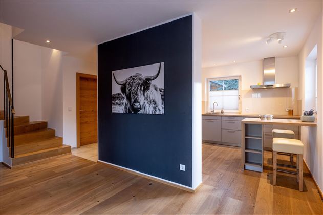 Ein modern gestalteter Wohnraum mit einer offenen Küche und Holzfußboden. An der Wand hängt ein großes Bild eines Highlands-Rinds.