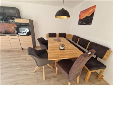 Ein stilvoller Essbereich mit einem großen Holztisch und gemütlichen Sitzbänken. Die moderne Küche im Hintergrund verleiht dem Raum eine einladende Atmosphäre.