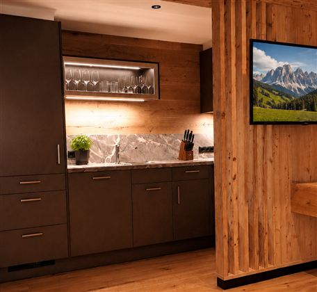 Eine moderne Küche mit dunklen Schränken und einer eleganten Marmortheke. An der Wand hängt ein Fernseher mit einem Bild von den Bergen.