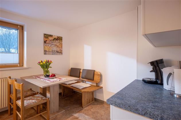 Eine helle und moderne Küche mit weißen Schränken und einem Fenster. Es gibt einen kleinen Tisch mit zwei Stühlen und eine einfache Arbeitsfläche.