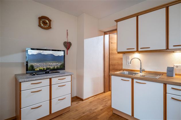 Eine moderne Küche mit hellen Möbeln und einem Fernseher. Der Raum hat einen warmen Holzboden und einen gemütlichen Eindruck.