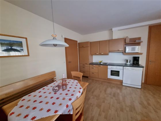 Een moderne keuken methouten kasten en een eettafel. Op de tafel ligt een rood-wit tafelkleed en een fles water.