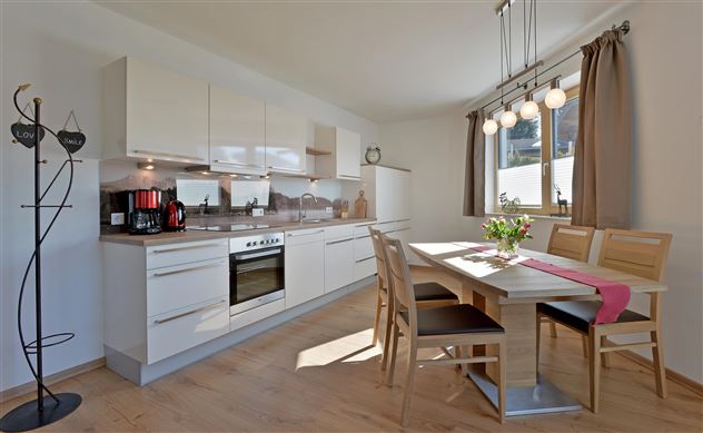 Eine moderne Küche mit hellen Möbeln und viel natürlichem Licht. Der Esstisch ist liebevoll gedeckt und bietet Platz für mehrere Personen.