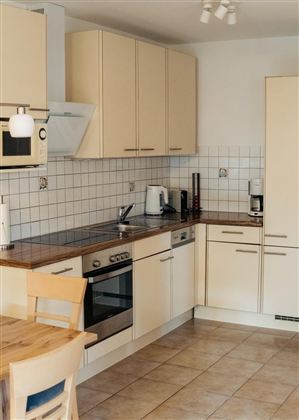 Eine moderne Küche mit hellen Schränken und einer Holzarbeitsplatte. Es gibt einen Essbereich mit einem Tisch und Stühlen.