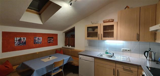 A cozy kitchen with a dining table and a seating area. Photos hang on the wall, and the light is friendly and inviting.