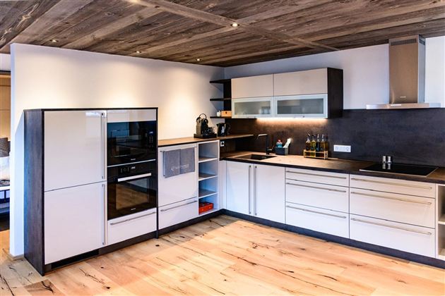 A modern kitchen with hardwood floors and elegant, minimalist furniture. The amenities include a refrigerator, an oven, and a sink.