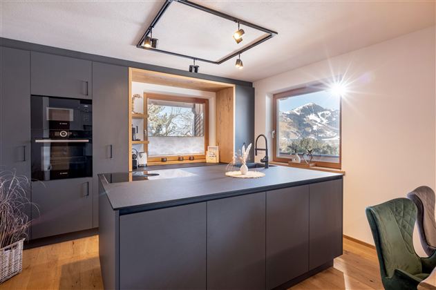 Modern kitchen with a black kitchen island and large windows offering a view of the mountains. Natural light pours in, creating an inviting atmosphere.