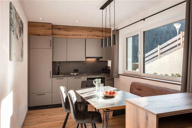 Eine moderne Küche mit einem Esstisch und Stühlen. Große Fenster lassen viel Licht herein und bieten einen Blick auf die Umgebung.