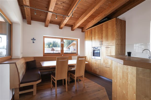 Moderne Küche mit Holzbalkendecke und großen Fenstern. Der Raum hat einen Essbereich mit eleganten Holzmöbeln und einer gemütlichen Atmosphäre.