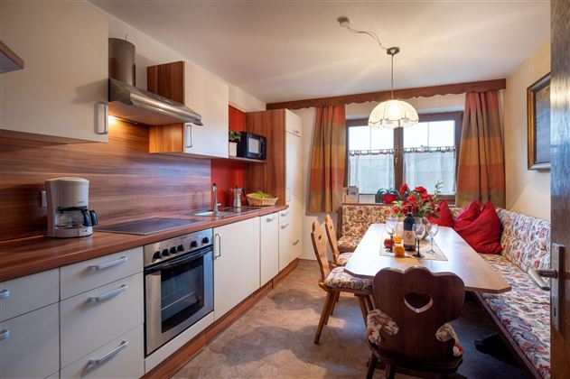 Eine moderne Küche mit Holzoberflächen und einer gemütlichen Essecke. Auf dem Tisch stehen Blumen und Getränke, der Raum ist hell und freundlich.