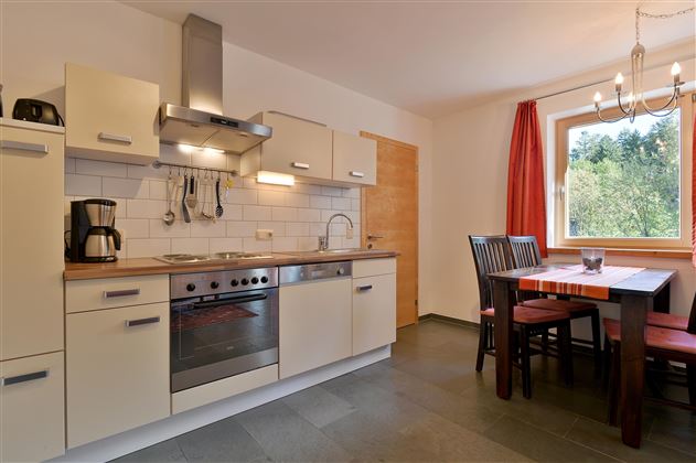 A modern kitchen with appliances and a dining area. Large windows provide plenty of daylight.