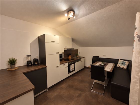Een moderne keuken met een combinatie van witte en donkere kasten. Een eetruimte met een tafel en zwarte stoelen aanvullen de ruimte.