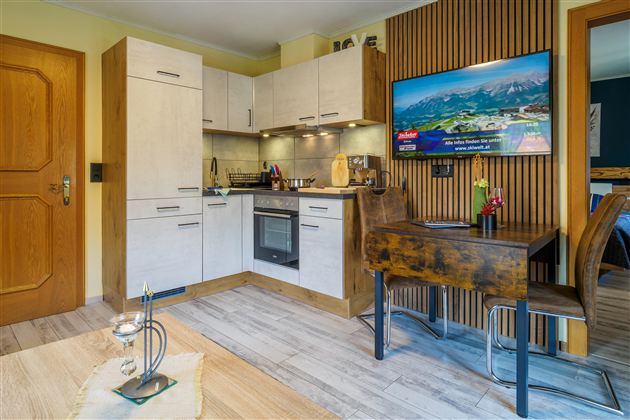 Eine moderne Küche mit Holz- und weißen Möbeln. Im Raum befindet sich ein Esstisch und ein Fernseher an der Wand.