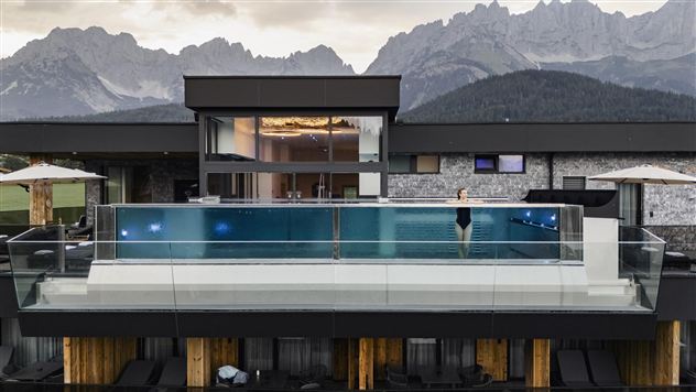 Een modern hotel met een infinitypool en een adembenemend berglandschap op de achtergrond. De architectuur is eigentijds en elegant.