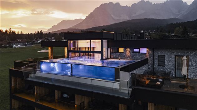 Een modern huis met een infinity-pool en een groot panoramisch uitzicht op de bergen. De sfeer is rustig, vooral bij zonsondergang.