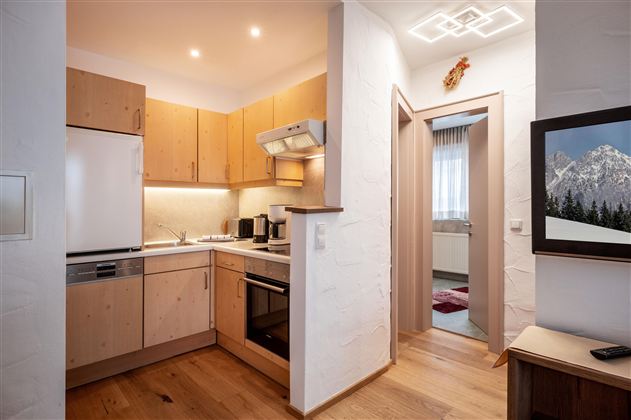 Eine moderne Küche mit Holzschränken und Geräten. Im Hintergrund ist ein Bild einer Berglandschaft sichtbar.