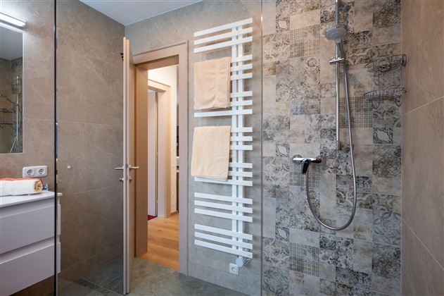 Ein modernes Badezimmer mit einer Dusche und einem Handtuchhalter. Die Wände sind mit dekorativen Fliesen verkleidet.