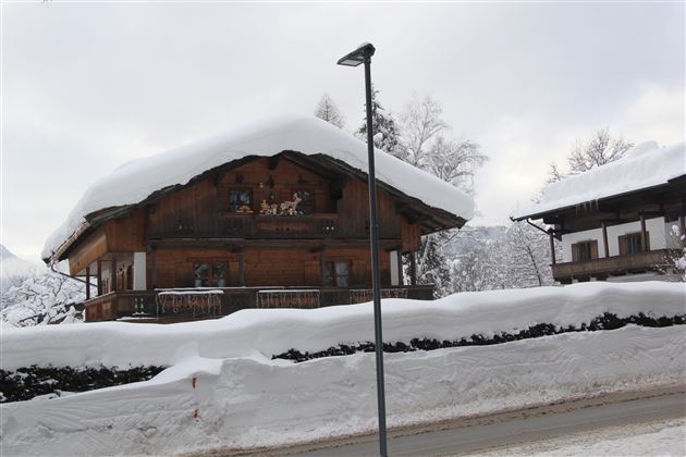 Ein traditionelles Holzhaus mit einem schneebedeckten Dach. Umgeben von Winterlandschaft und frischem Schnee.
