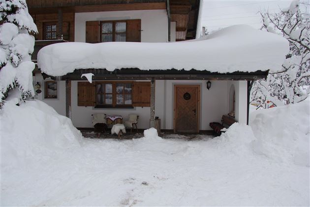Eine verschneite Fassade eines Hauses mit dicken Schneeverwehungen. Der Eingang ist gut sichtbar, jedoch von Schnee umgeben.