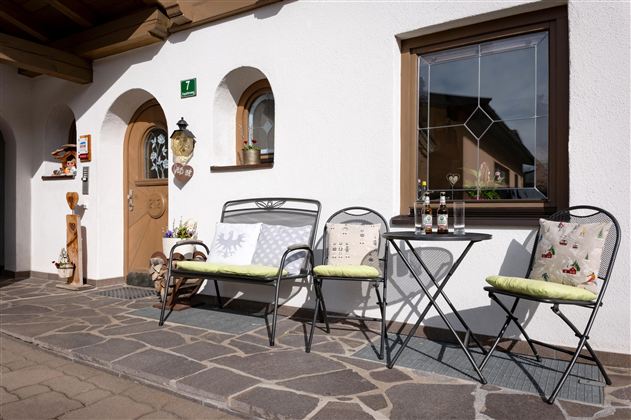 A cozy terrace with an entrance and a small table. There are two colorful benches and a friendly, inviting atmosphere.