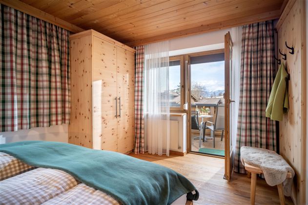 A cozy bedroom with a wooden ceiling and checked curtains. The balcony offers a view of the surroundings and fresh air.
