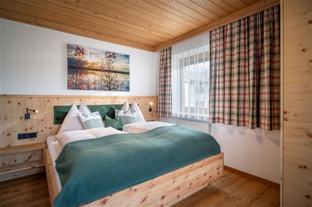 A cozy bedroom with a double bed and wood paneling. The room has a window with curtains and a picture on the wall.