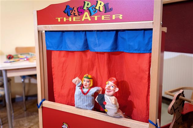 A puppet theater with colorful puppets is on a table. The puppets depict a Kasper and a girl who are waiting for a performance.