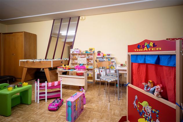 A colorful play area with various toys, including a puppet theater and a pool table. The walls are bright, and the room feels welcoming for children.