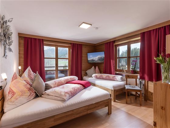 Ein gemütliches Schlafzimmer mit zwei Einzelbetten und bunten Kissen. Große Fenster bieten einen Blick auf die Natur und erlauben viel Tageslicht.