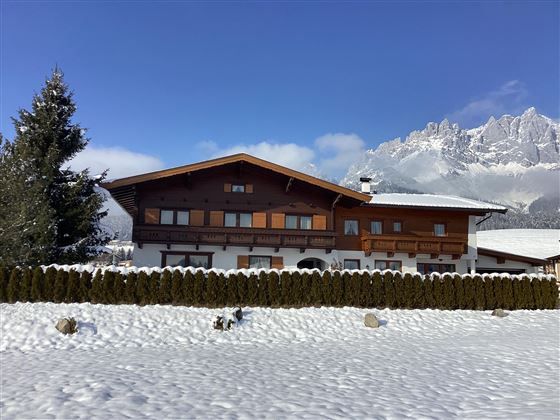Ein charmantes Haus im Winter mit Schnee bedeckt. Im Hintergrund sind majestätische Berge zu sehen.