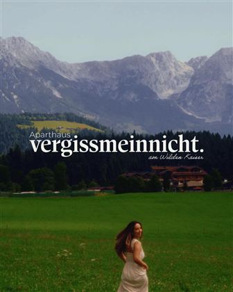 A beautiful old building amid a picturesque mountain landscape. In the foreground stands a woman in a long dress.
