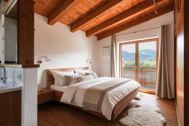 Ein modernes Schlafzimmer mit Holzdecke und großen Fenstern. Der Raum ist hell und lädt zur Entspannung ein und bietet eine schöne Aussicht auf die Landschaft.