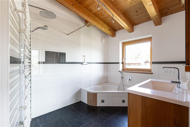 Ein modernes Badezimmer mit einer Dusche und einer Badewanne. Die Holzbalkendecke verleiht dem Raum eine warme Atmosphäre.