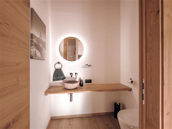 Ein modernes Badezimmer mit einer Holzoberfläche und einer runden Spiegelleuchte. Die Einrichtung ist minimalistisch mit einem Waschbecken und einer toilet.