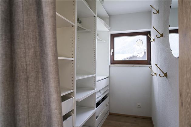 Een moderne ruimte met witte planken en een raam. Aan de muur zijn enkele haken voor kleding bevestigd.
