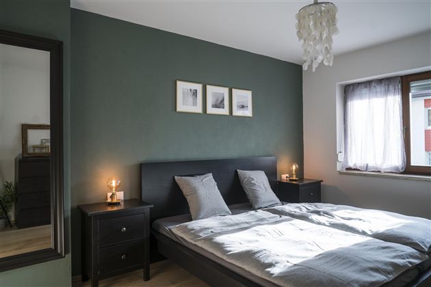 Een moderne slaapkamer met een tweepersoonsbed en zachte kleuren. Er zijn nachtkastjes met lampen en foto's aan de muur.