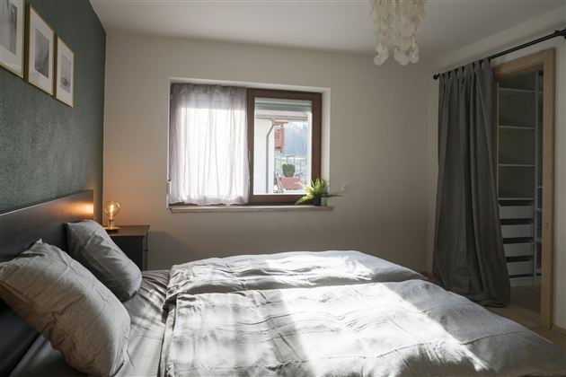Een lichte slaapkamer met een twijfelaar en zachte kussens. Naast het raam staan planten, en de muren zijn in neutrale kleuren geschilderd.