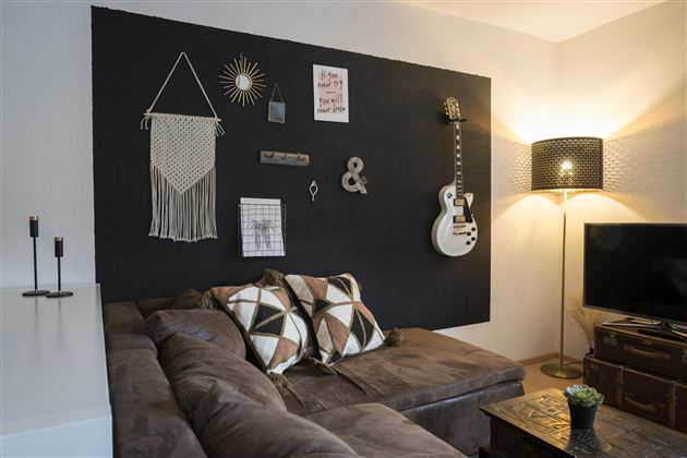 Een stijlvolle woonkamer met een donkere muur, decoratieve elementen en een comfortabele bank. Een gitaar en een lamp geven de ruimte een uitnodigende sfeer.