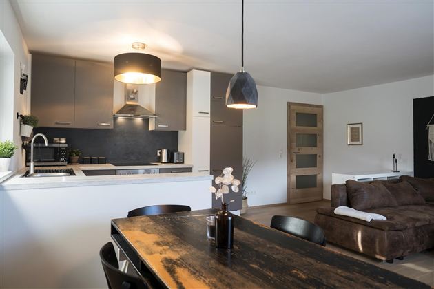 Een moderne keuken met een grote eettafel en een gezellig bank. De ruimte is licht en vriendelijk ingericht.
