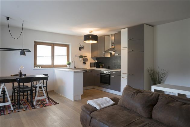 Een moderne woning met een open keuken en een eetgedeelte. De ruimte is licht en vriendelijk ingericht met een comfortabele bank.