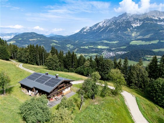 Ein malerisches Holzhaus mit Solarpanelen in den Bergen. Die Landschaft ist grün und üppig mit einem Blick auf majestätische Berge.