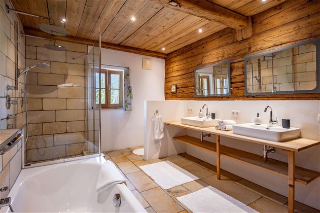 Ein modernes Badezimmer mit Holzverkleidung und zwei Waschbecken. Die Dusche ist durch eine Glasabtrennung getrennt und der Raum ist hell und einladend.