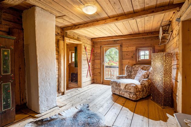 Ein rustikales Zimmer mit Holzwänden und einem gemütlichen Sessel. Ein Fenster bietet Blick auf die Natur draußen.