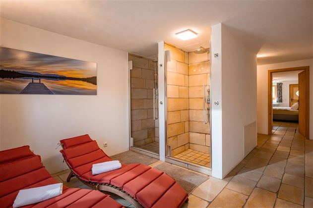 Ein modernes Badezimmer mit zwei Duschkabinen und roten Liegen. An der Wand hängt ein Bild von einem Sonnenuntergang am Wasser.