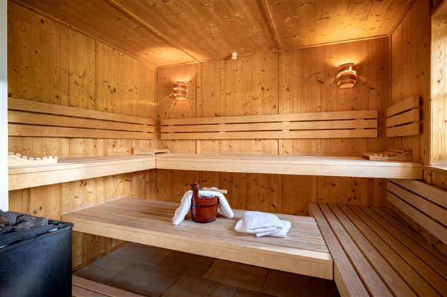 Eine helle Sauna mit Holzregalen und sanftem Licht. Handtücher und ein Holzbehälter stehen bereit.
