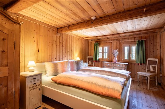 Ein gemütliches Schlafzimmer mit Holzwänden und zwei Betten. Sanfte Beleuchtung und grüne Vorhänge schaffen eine einladende Atmosphäre.