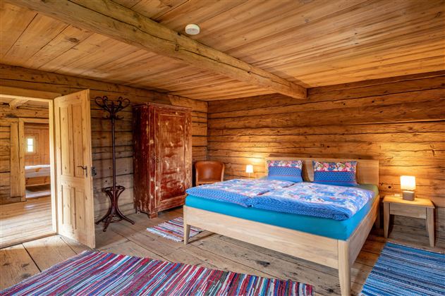 Ein gemütliches Schlafzimmer mitHolzdecke und Wänden. Das Zimmer verfügt über ein großes Bett, einen Stuhl und einen Kleiderschrank.