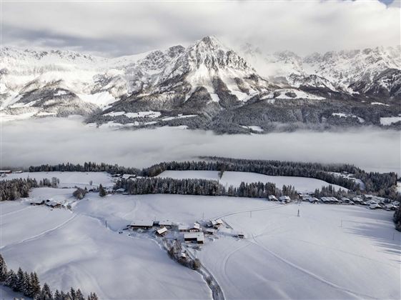 Eine schneebedeckte Landschaft mit hohen Bergen im Hintergrund. Der Himmel ist bewölkt und es gibt Nebel über den Feldern.