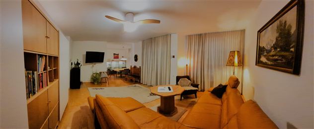 A modern living room with a beige sofa, a coffee table, and a floor lamp. The walls are light, and large windows with curtains provide plenty of daylight.