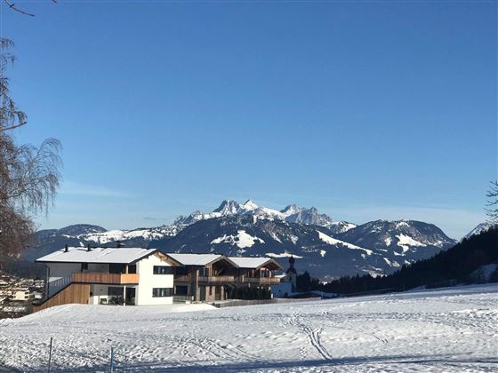 A beautiful winter landscape with snow-covered meadows and impressive mountains in the background. The clear, blue sky completes the scene.